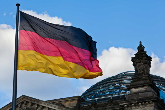 German,Reichstag,Dome,With,The,German,National,Flag German flag waving against a blue sky near a historic building