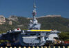 A naval ship docked near a mountainous coastline