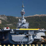 A naval ship docked near a mountainous coastline