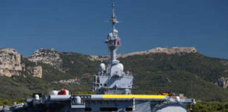A naval ship docked near a mountainous coastline