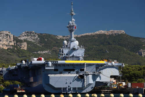 A naval ship docked near a mountainous coastline