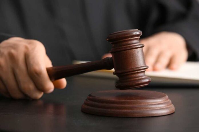 Male,Judge,With,Gavel,At,Table,In,Courtroom A judge's hand holding a gavel above a wooden block