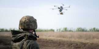 A soldier observing a drone flying over a field