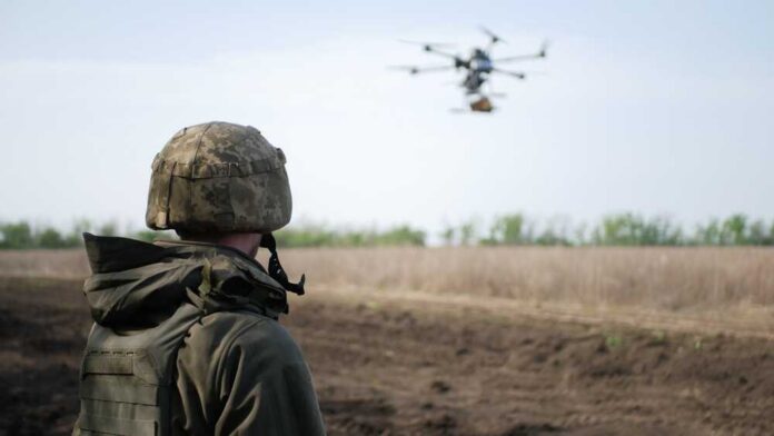 A soldier observing a drone flying over a field