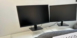 An office desk with two computer monitors and a chair labeled 'REPLACED BY AI'