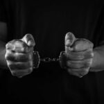 Alleged Killer Charged: Was It a Job Trap? Hands holding handcuffs in a black and white image