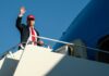 A man in a suit and red cap waving from the steps of an airplane