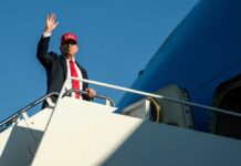 A man in a suit and red cap waving from the steps of an airplane