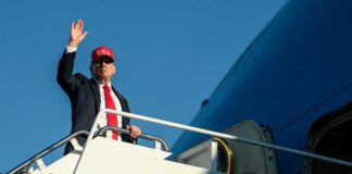 A man in a suit and red cap waving from the steps of an airplane
