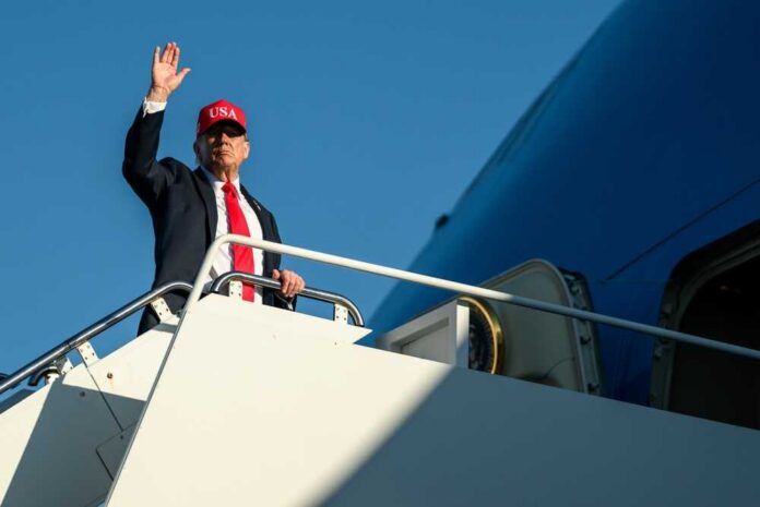 A man in a suit and red cap waving from the steps of an airplane
