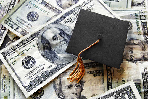 A graduation cap placed on a pile of U.S. dollar bills