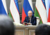 Wounded Russia’s Nuclear RISK – Unstable and Armed man in suit speaking at a conference table with microphones and flags behind