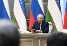 Wounded Russia’s Nuclear RISK – Unstable and Armed man in suit speaking at a conference table with microphones and flags behind