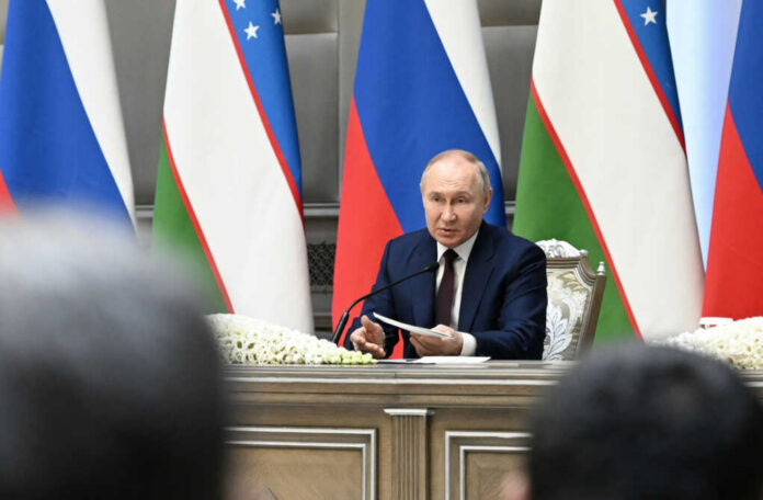 vladimir-putin2495936647jpg man in suit speaking at a conference table with microphones and flags behind