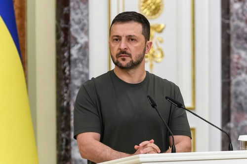 Man speaking at podium with microphones, Ukrainian flag behind.