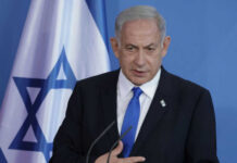 Man speaking in front of Israeli flag backdrop
