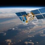 Pentagon Bets on Anti-Jam Swarm A satellite equipped with solar panels orbiting above the Earth, surrounded by clouds