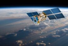 Pentagon Bets on Anti-Jam Swarm A satellite equipped with solar panels orbiting above the Earth, surrounded by clouds