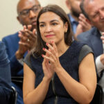 AOC Targets Amazon, Facebook Power Woman clapping at an indoor event