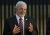Elderly man in suit speaking with hands raised