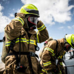 Inmates On The Frontlines — California Cashes In On Captive Crews Firefighters in protective gear standing outside cloudy sky