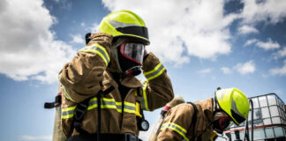 Firefighters in protective gear standing outside cloudy sky