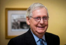 Power Vacuum Brewing? McConnell Hospitalized—Again Smiling man in suit with round glasses indoors.