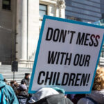 Parents Shut Out? Judge Lets Bombshell Case Roll Protest sign held at a rally in an urban square