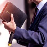 Devil ‘Shot’ On Stage—Media Erupts A person in formal attire holding a Bible while speaking
