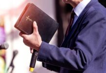 Devil ‘Shot’ On Stage—Media Erupts A person in formal attire holding a Bible while speaking