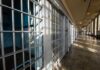 Interior view of a prison corridor with jail cells and sunlight streaming through windows