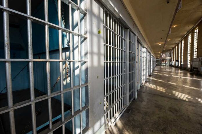 Sun,Shining,On,The,Bars,Of,A,Historic,Prison Interior view of a prison corridor with jail cells and sunlight streaming through windows