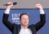 Warren Moves To Stall Musk’s Moonshot Person with a microphone raising hands in celebration