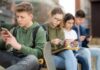 Group of teenagers sitting outdoors, focused on their devices