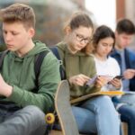 Quiet Reliance: Kids Confide In Bots Group of teenagers sitting outdoors, focused on their devices