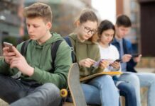 Group of teenagers sitting outdoors, focused on their devices