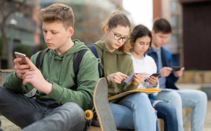 Teenage,Friends,Spending,Time,Together,On,Streets,Of,City,,Messaging Group of teenagers sitting outdoors, focused on their devices