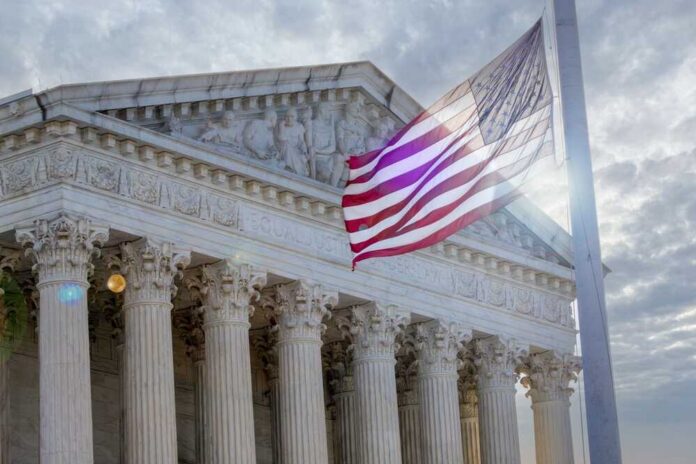 The,Sun,Peaks,Through,Clouds,To,Stream,Through,American,Flag The Supreme Court building with an American flag waving in front