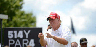 Man in red cap and white golf shirt gesturing at a golf event