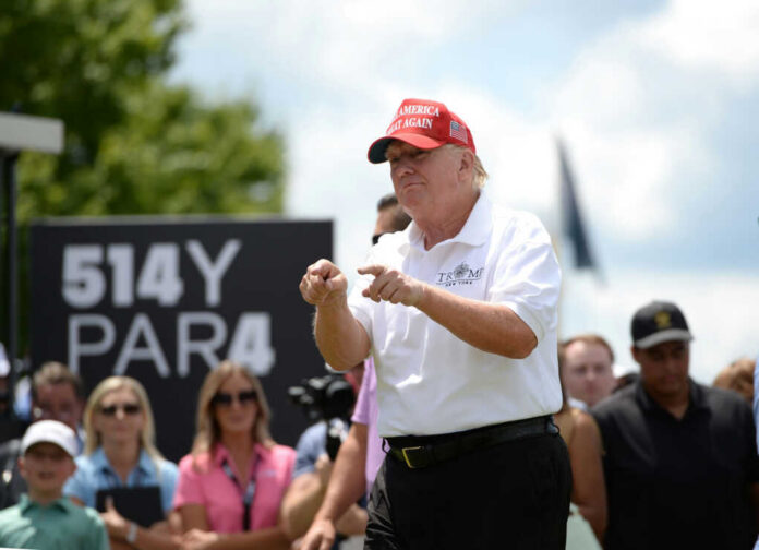 Man in red cap and white golf shirt gesturing at a golf event