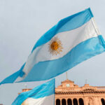 Argentinian flag with sun emblem waving above a historic building