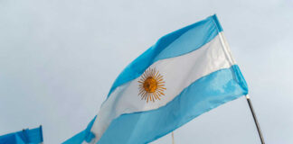 Argentinian flag with sun emblem waving above a historic building
