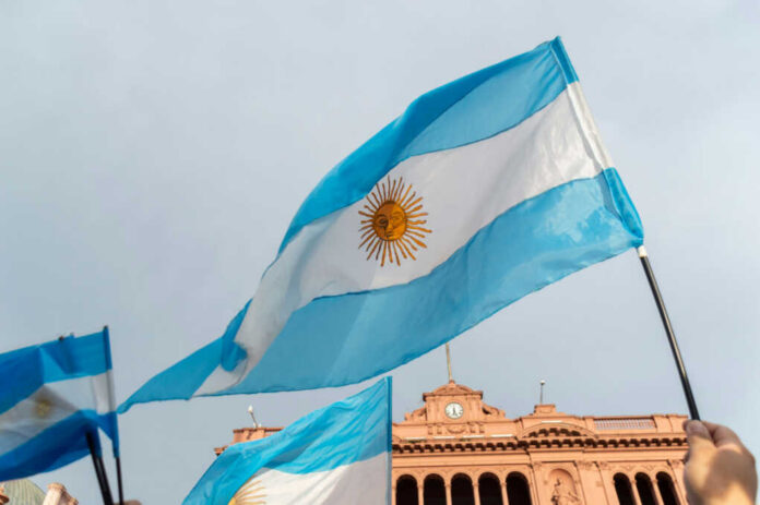 Argentinian flag with sun emblem waving above a historic building