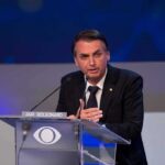 Bolsonaro Dynasty Reloads Against Lula man in suit speaking at a podium