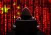 Hooded figure using a laptop against a red digital code background