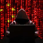 Pentagon Red Flag: China Inside Our Chips? Hooded figure using a laptop against a red digital code background