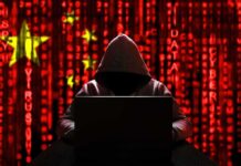 Hooded figure using a laptop against a red digital code background