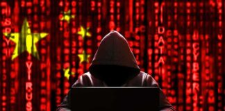 Hooded figure using a laptop against a red digital code background