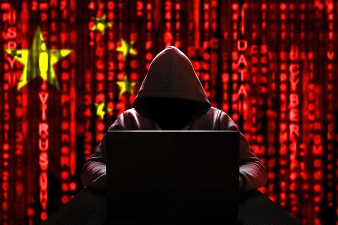 Hooded figure using a laptop against a red digital code background