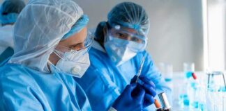 Scientists in protective gear working with a syringe in a laboratory